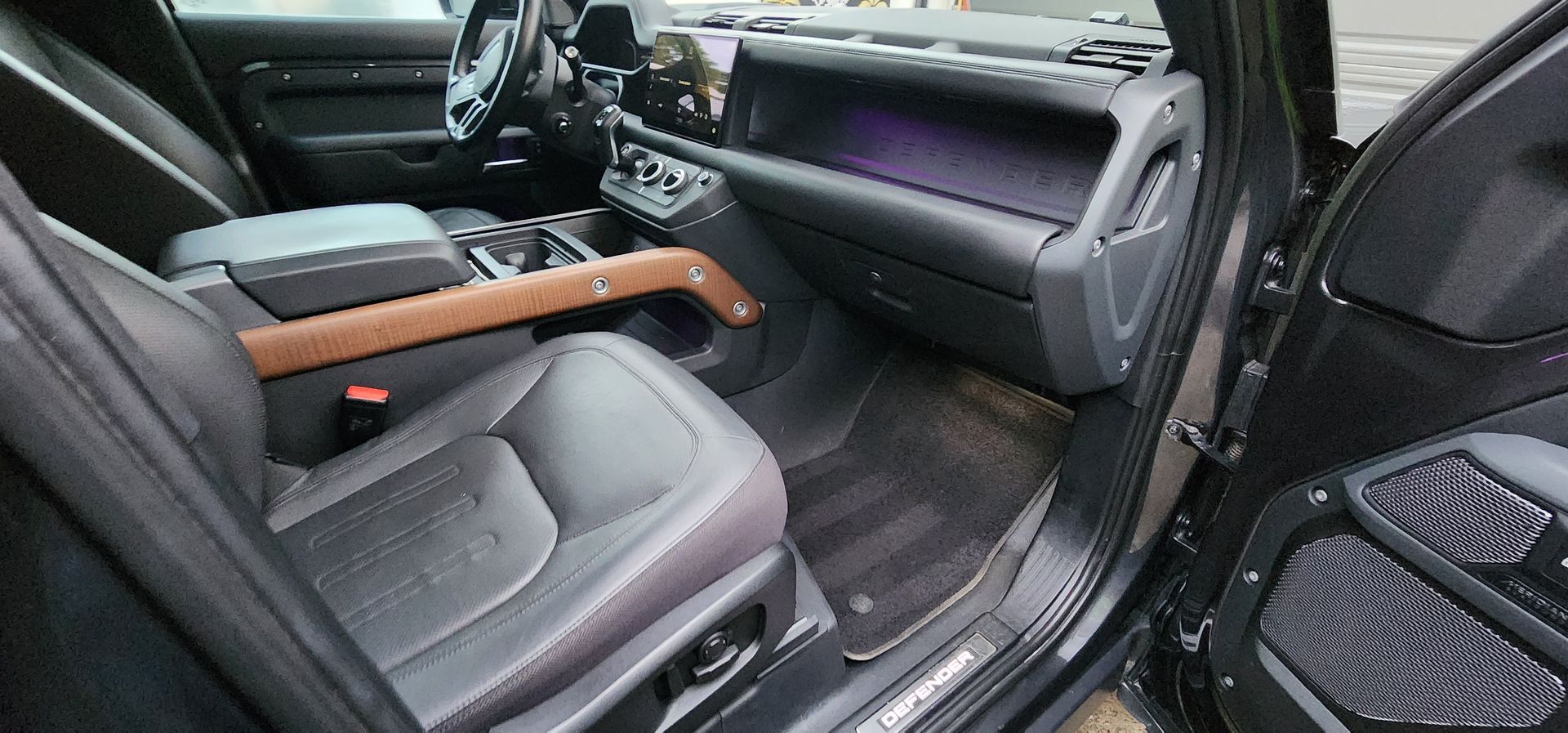 Car interior with black leather seats and a brown wooden armrest across the center console.