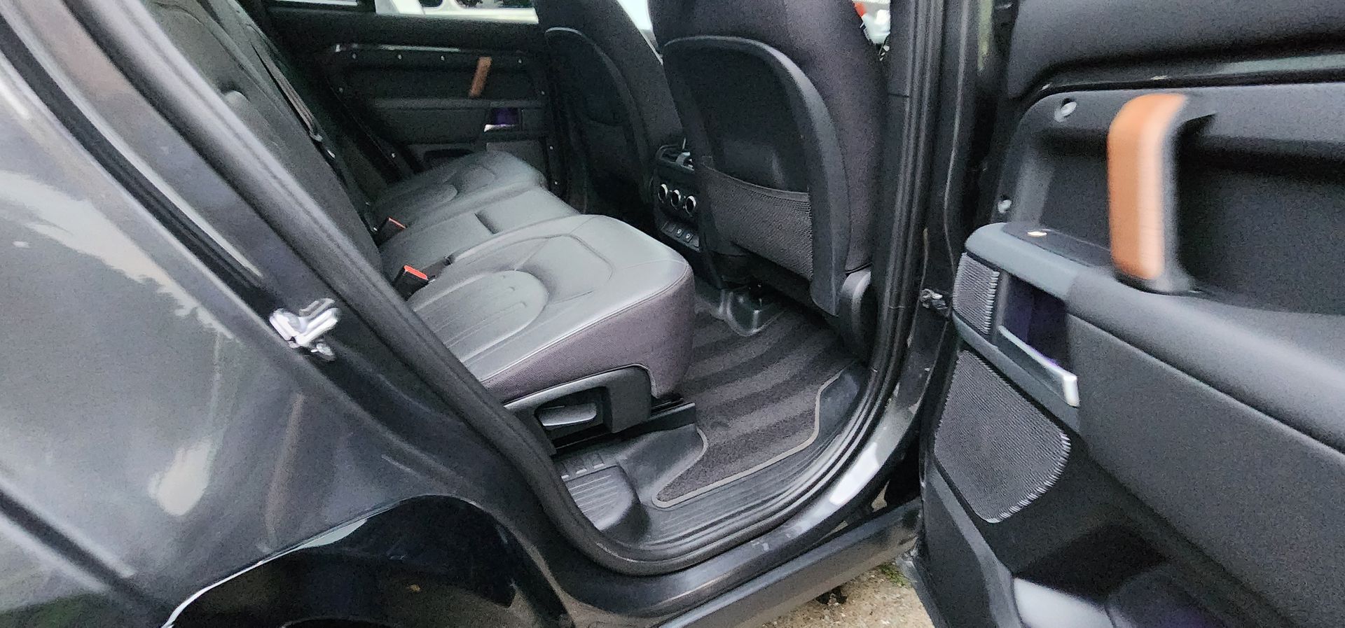 Car interior with rear door open, showing black seats and the back seat floor area.