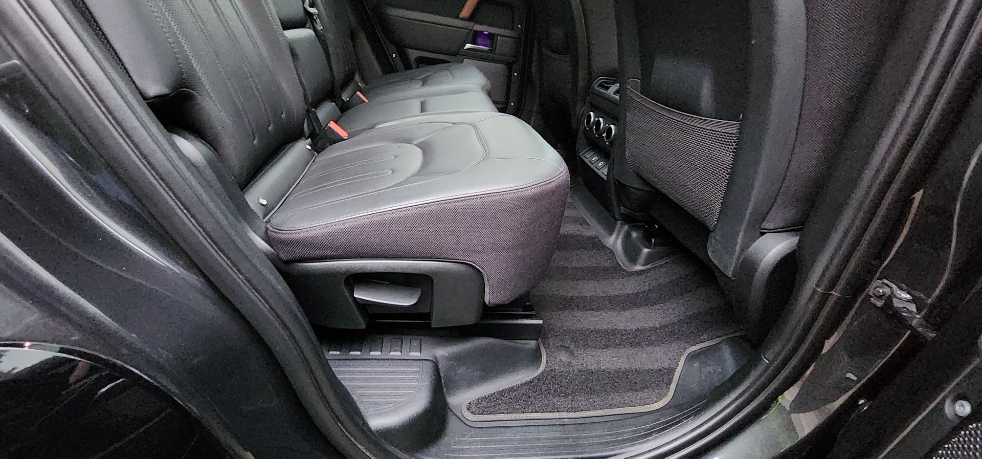 Black leather car interior with a folded rear seat and floor mat visible.