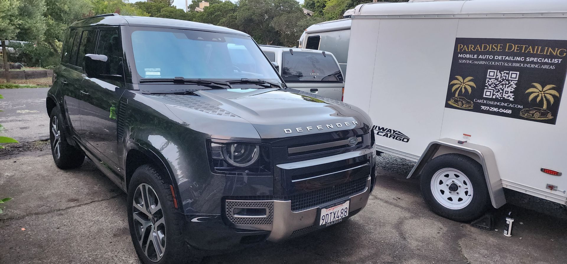 Black SUV parked nose-to-nose with a white trailer in a lot, with another vehicle behind.