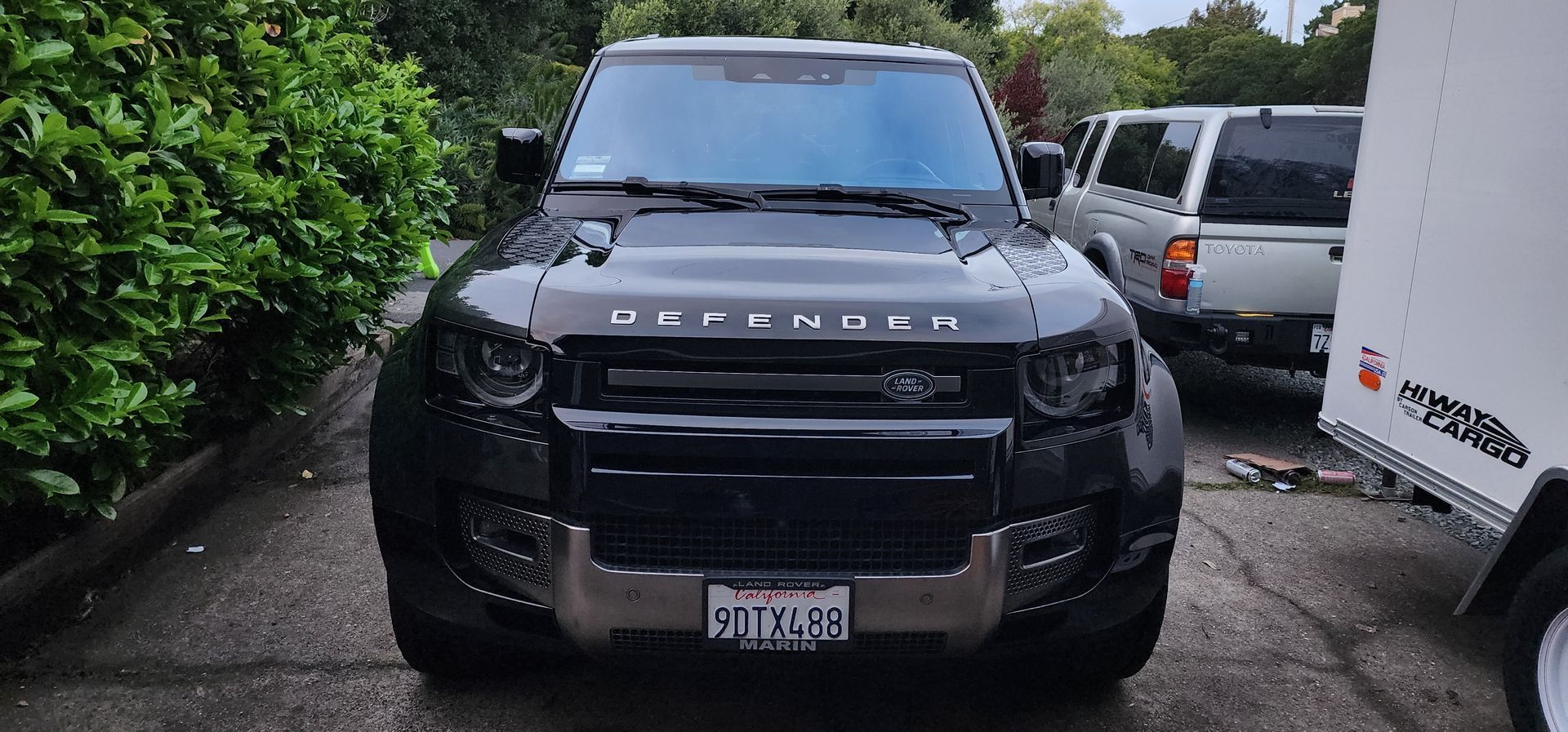 Black Land Rover parked in a tight space, front view with other vehicles beside it.