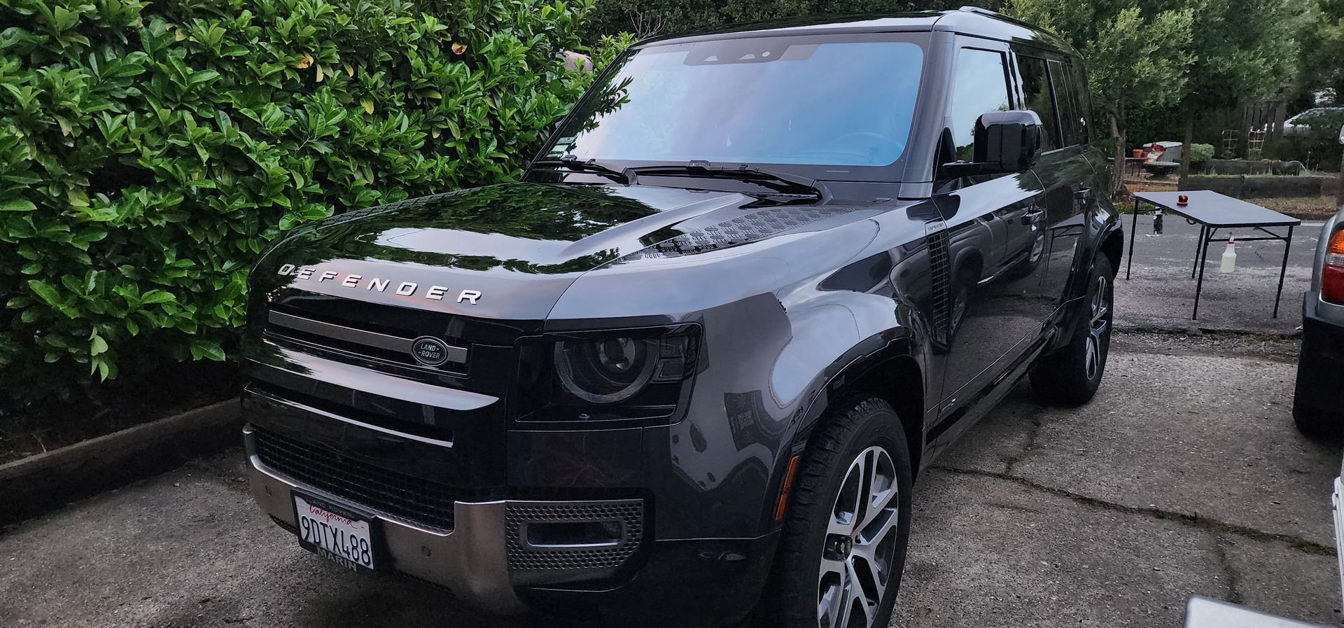 Black Land Rover SUV parked in a driveway beside greenery, wet pavement visible