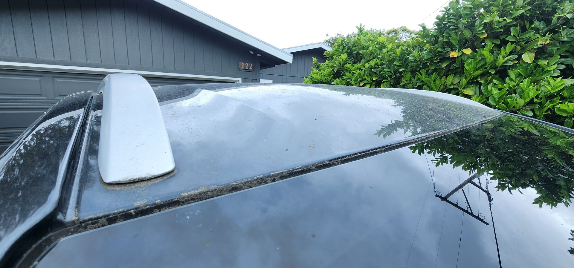 White shark fin antenna on the roof of a black car with rain droplets near a house