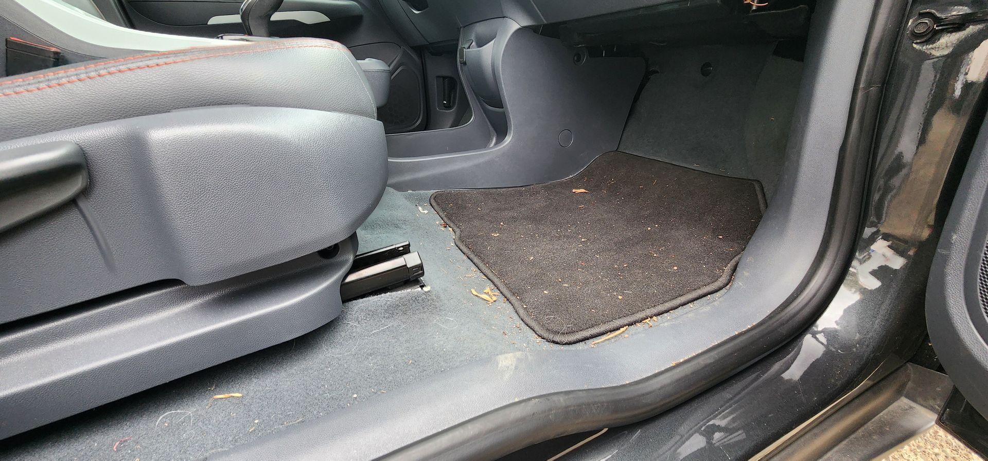 Car interior with folded rear seat, open door, and floor mats on gray upholstery