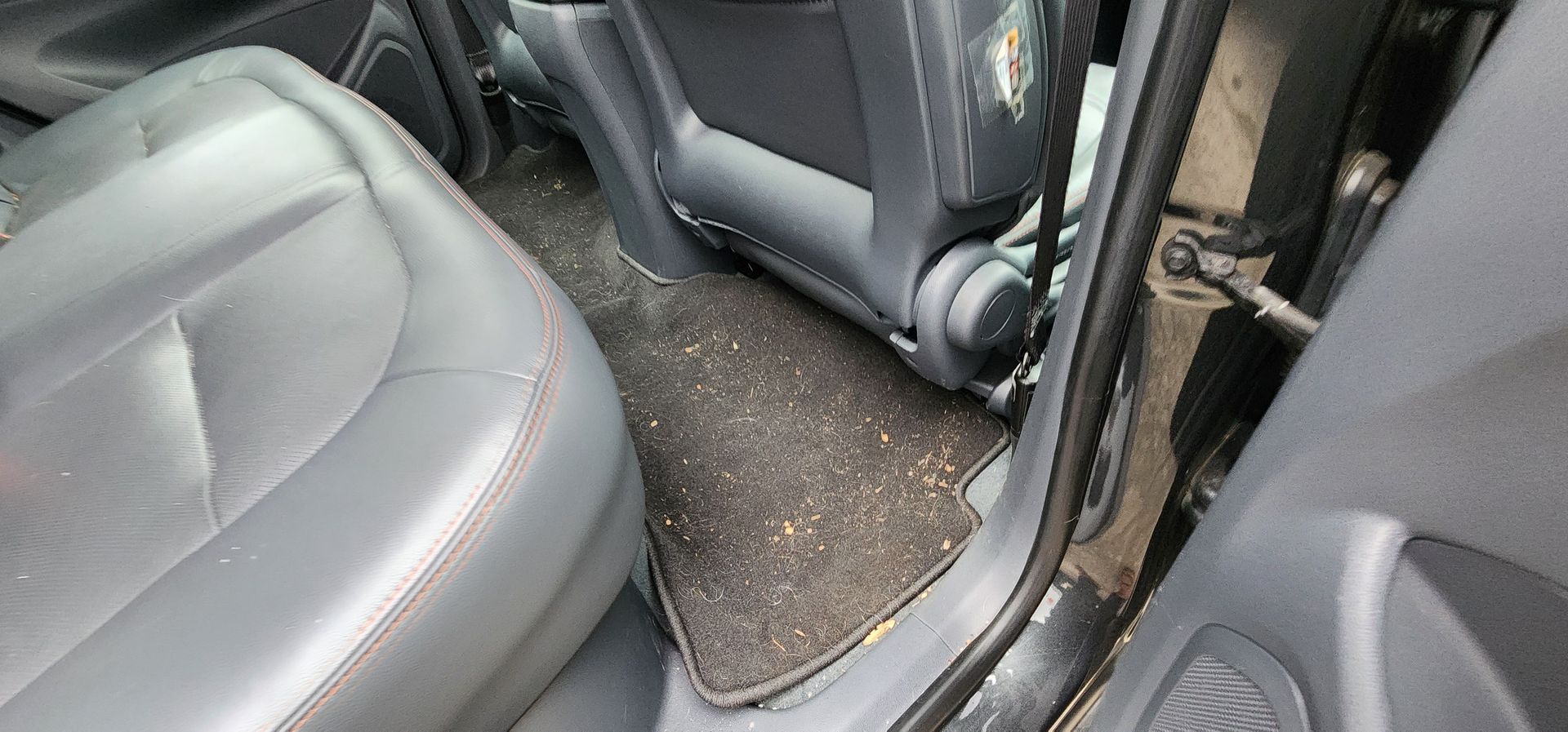 Car interior with open rear door and dirty floor mat between gray seats