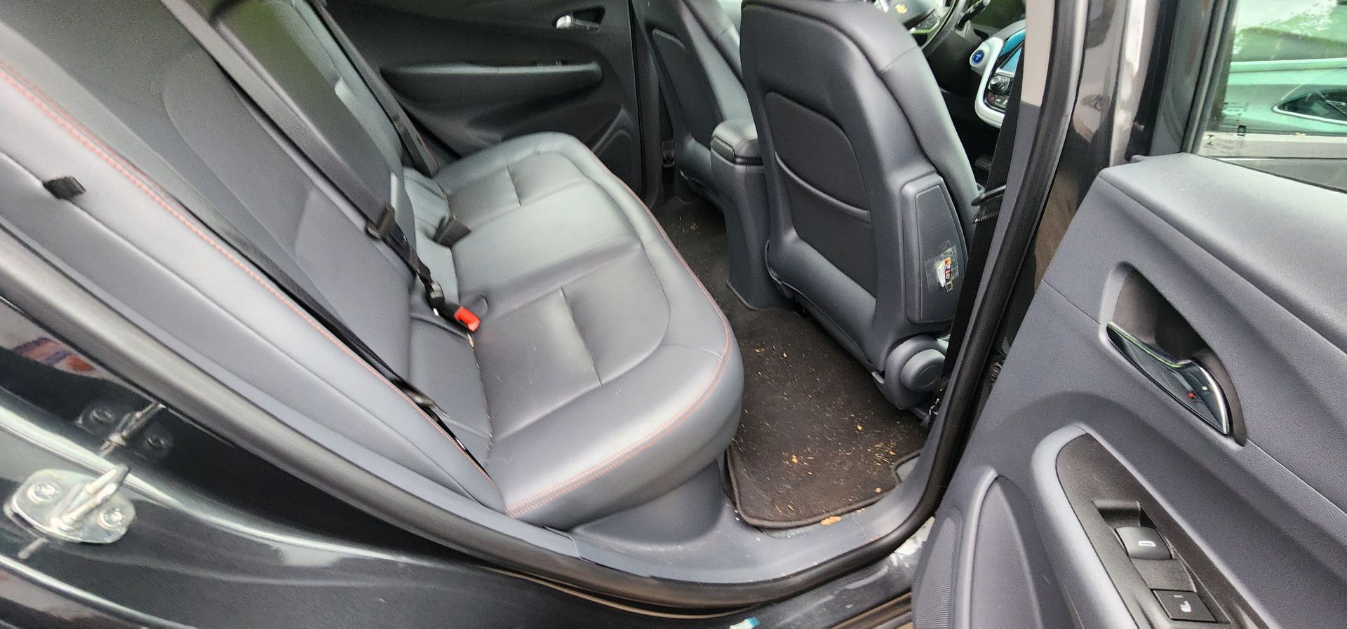 Car interior with gray seats and an open rear door, showing the back seat and floor area