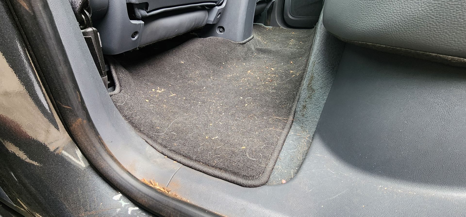 Car seat footwell with black upholstery and gray carpet, showing the lower side of a vehicle interior