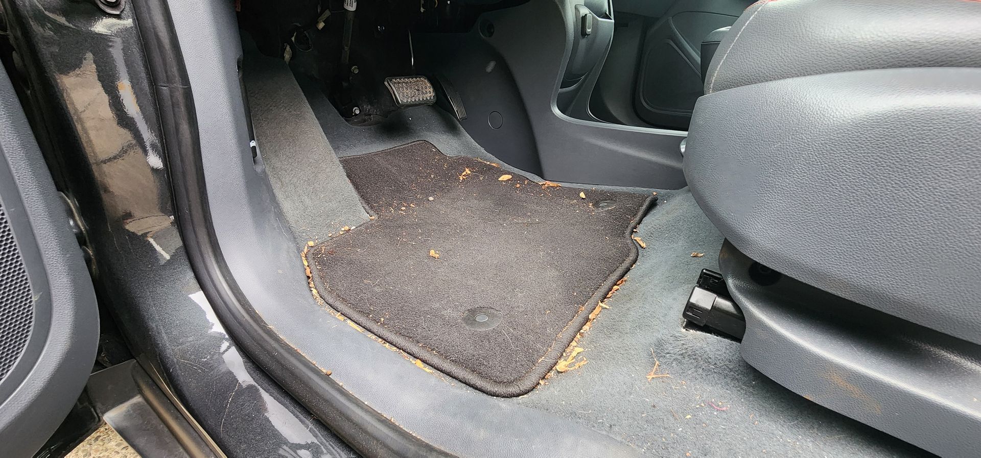 Car floor mat with dirt and debris near the seat and door sill