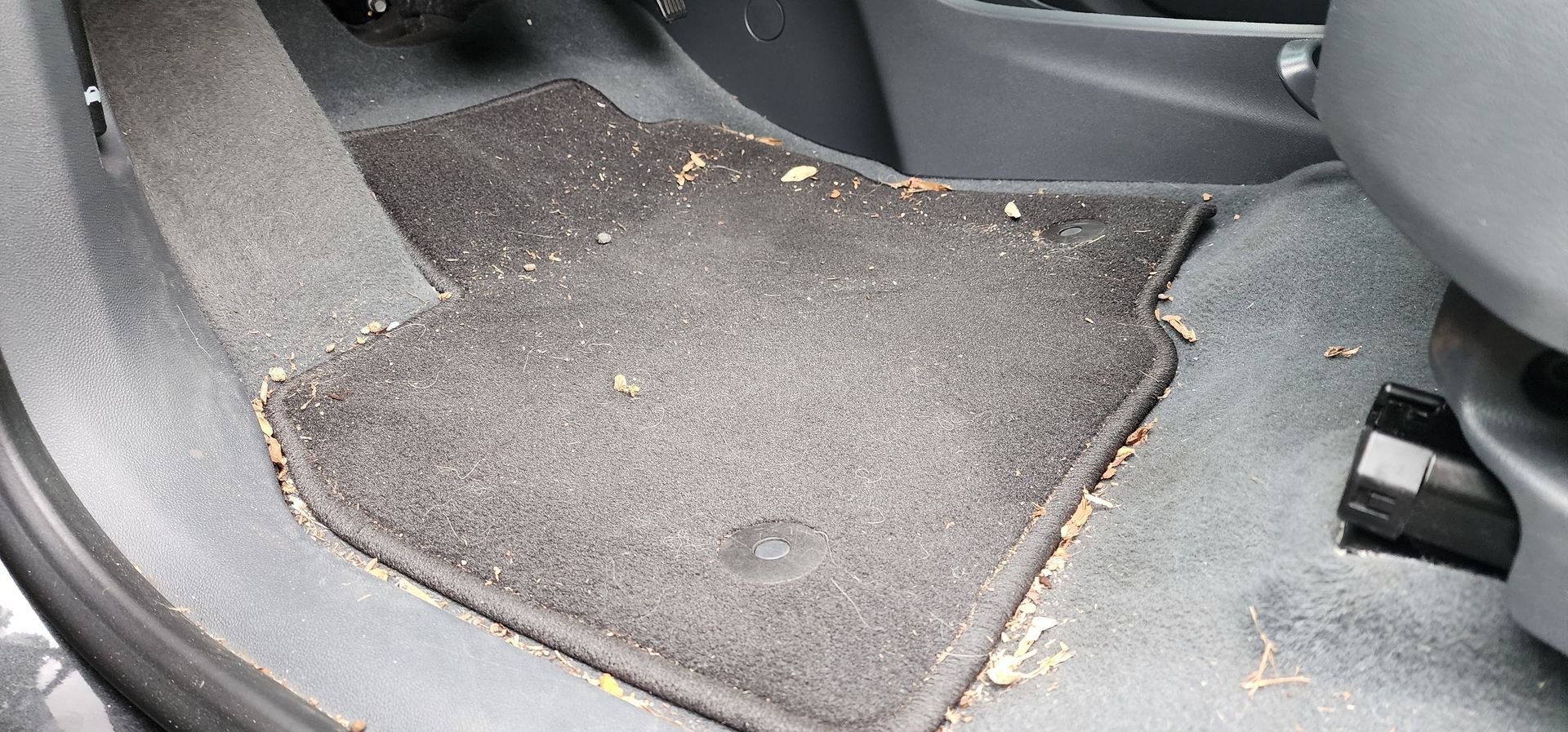 Dirty gray car floor mat with crumbs and debris on the rear seat floor.