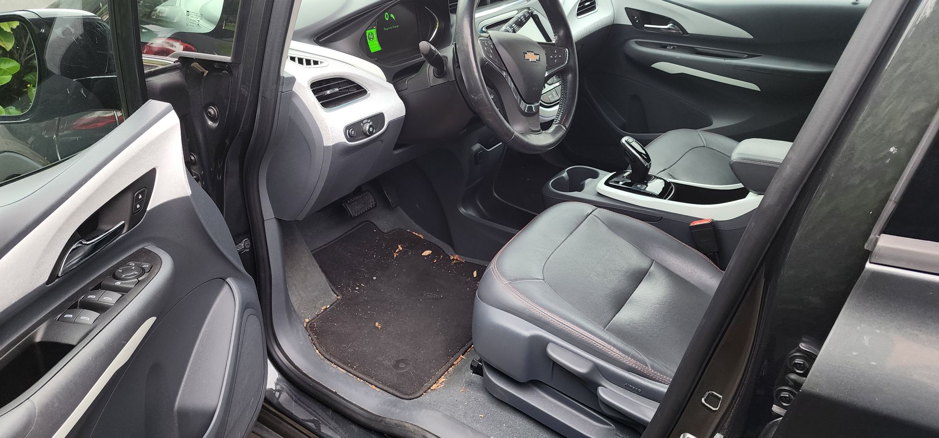 Open car door showing the front seats, dashboard, and steering wheel of a dark interior.