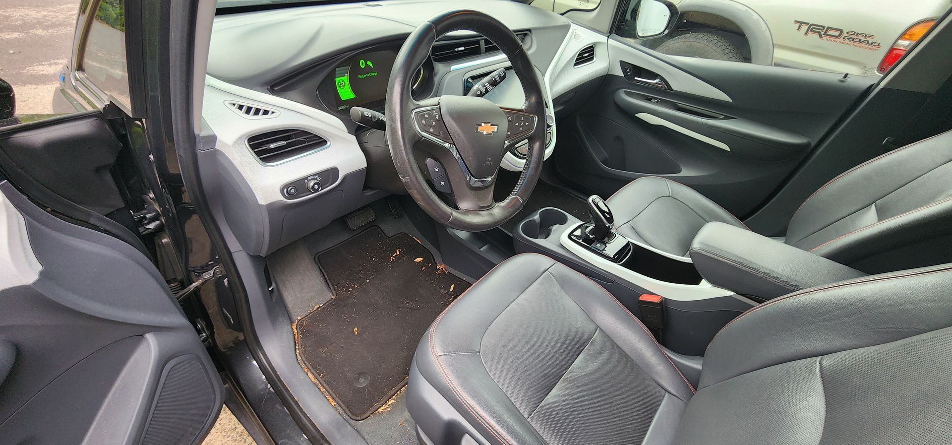 Car interior with black seats, steering wheel, center console, and an open driver’s door
