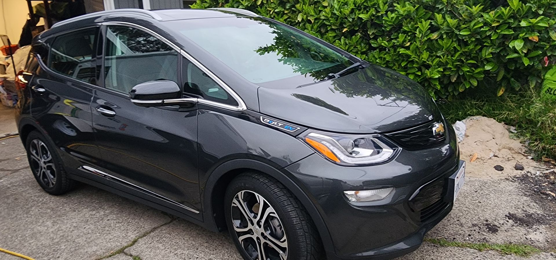 Black compact SUV parked on a driveway beside green hedges, front-left view