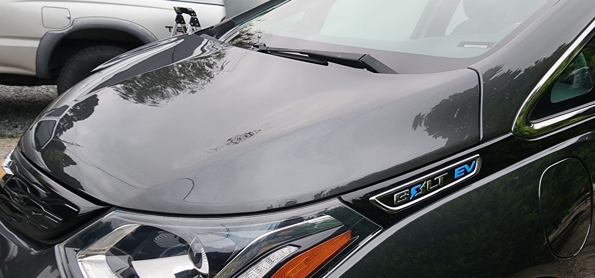 Close-up of a black car hood and grille with a blue badge, parked beside a silver vehicle
