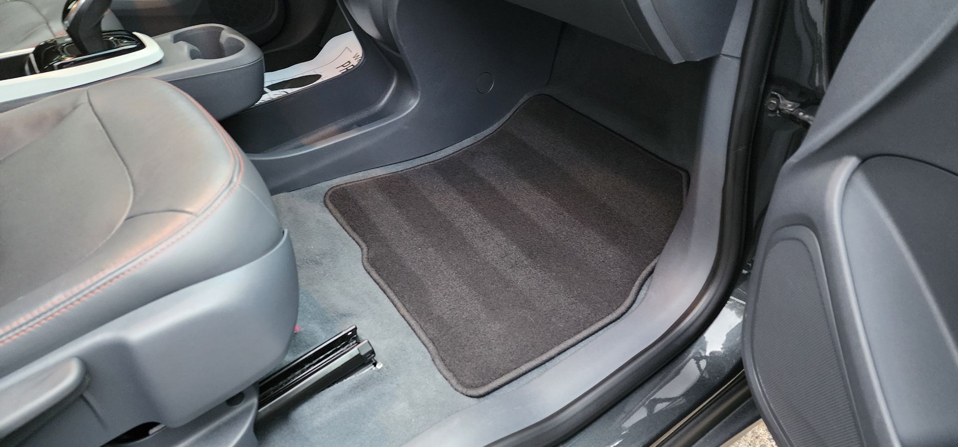 Car interior with gray seats and dark floor mats, showing the rear passenger footwell and door sill.