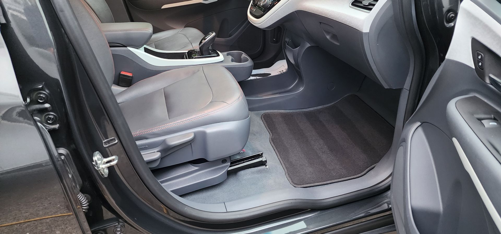 Open car door showing gray front seat, black floor mats, and center console.
