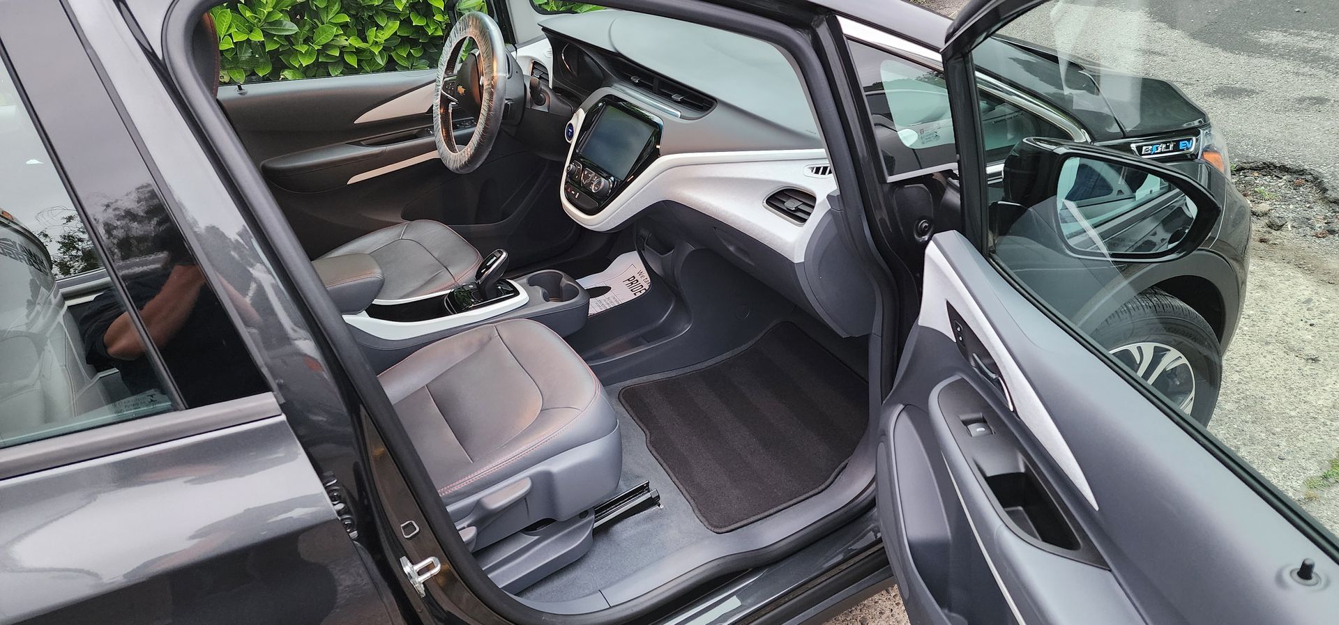 Open car door showing a gray interior, steering wheel, and front seats in a showroom-like setting