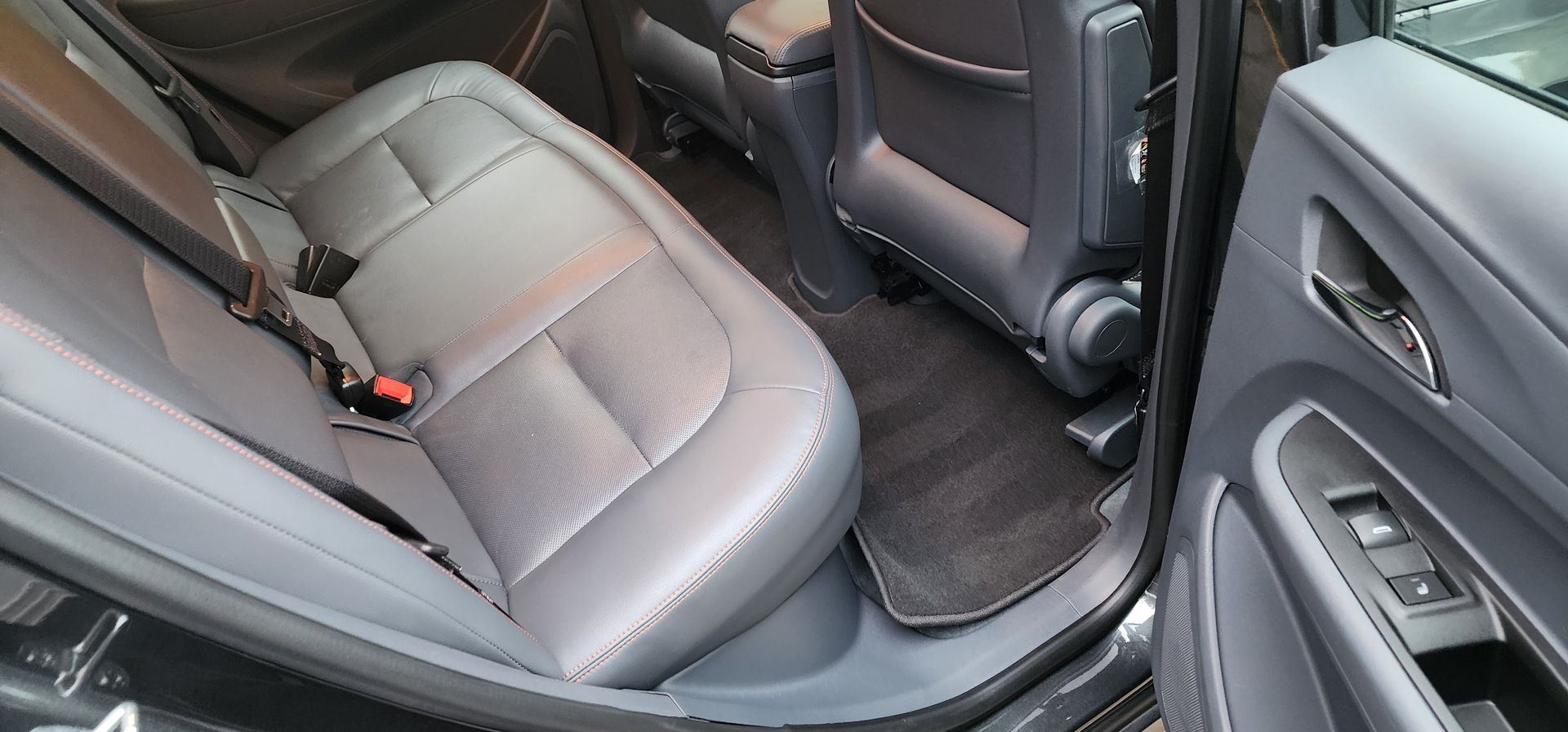 Rear passenger seat area of a car with gray upholstery and black floor mats