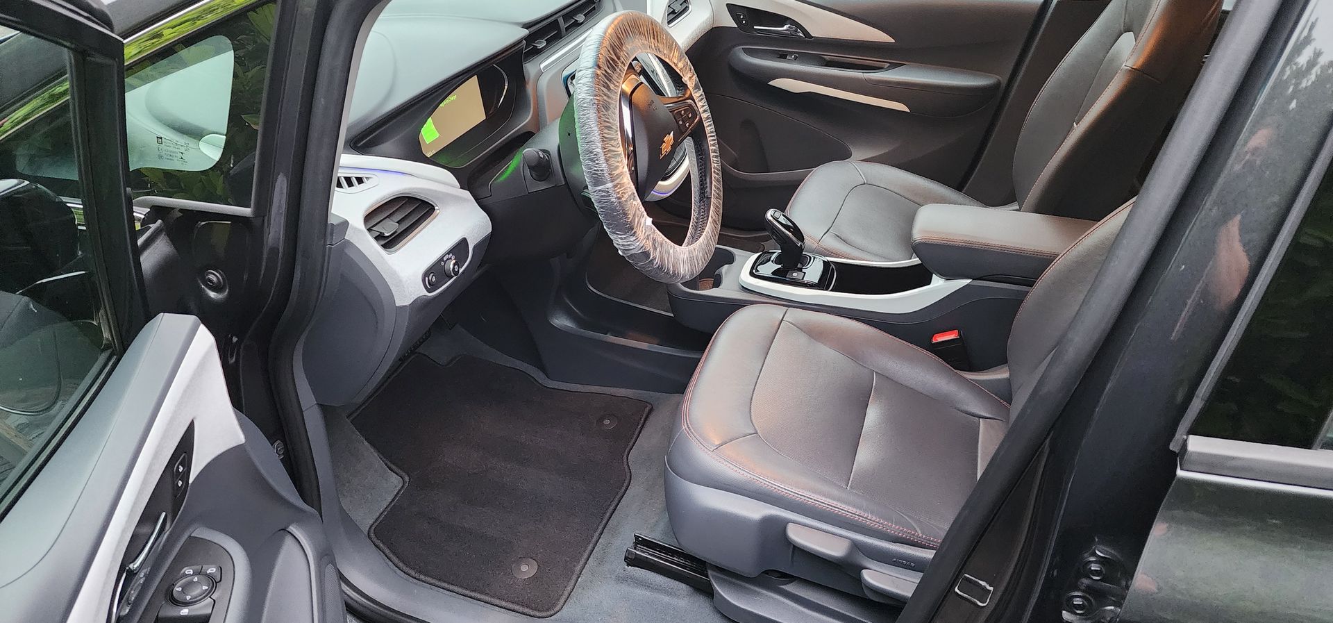 Open car door showing black interior with tan-trimmed steering wheel and front seat