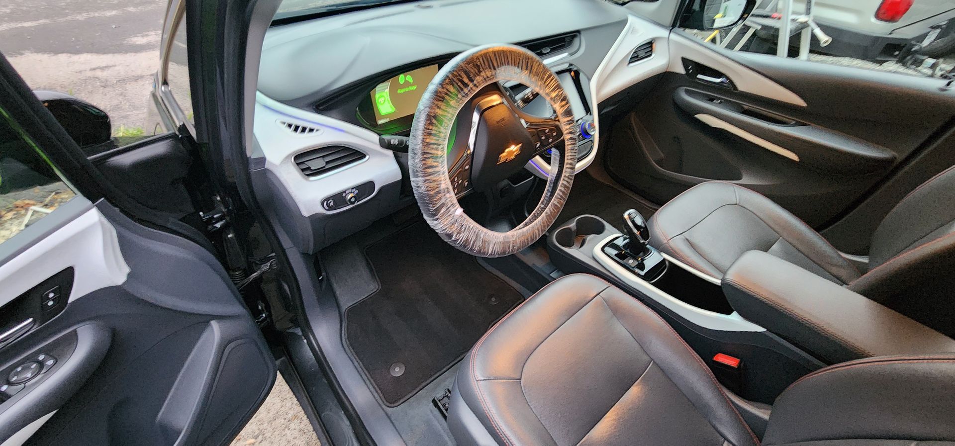 Car interior with black leather seats, illuminated steering wheel, and open driver’s door; dashboard visible