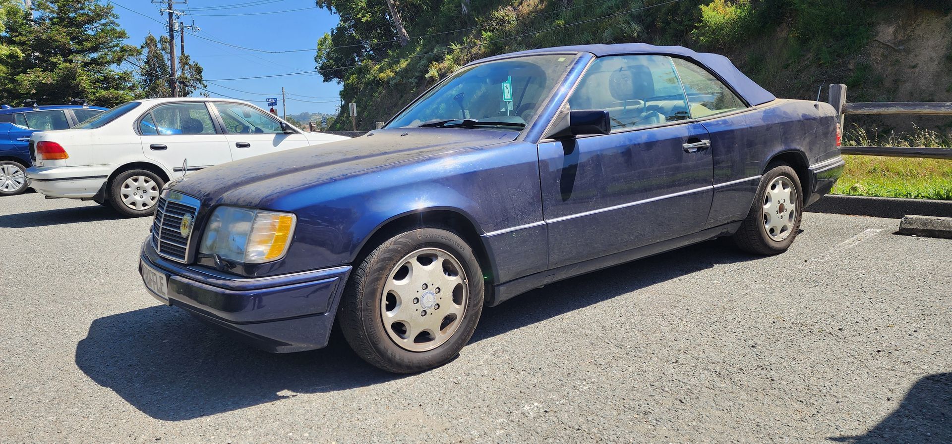 Blue sedan parked on gravel with a white car in the background on a sunny day