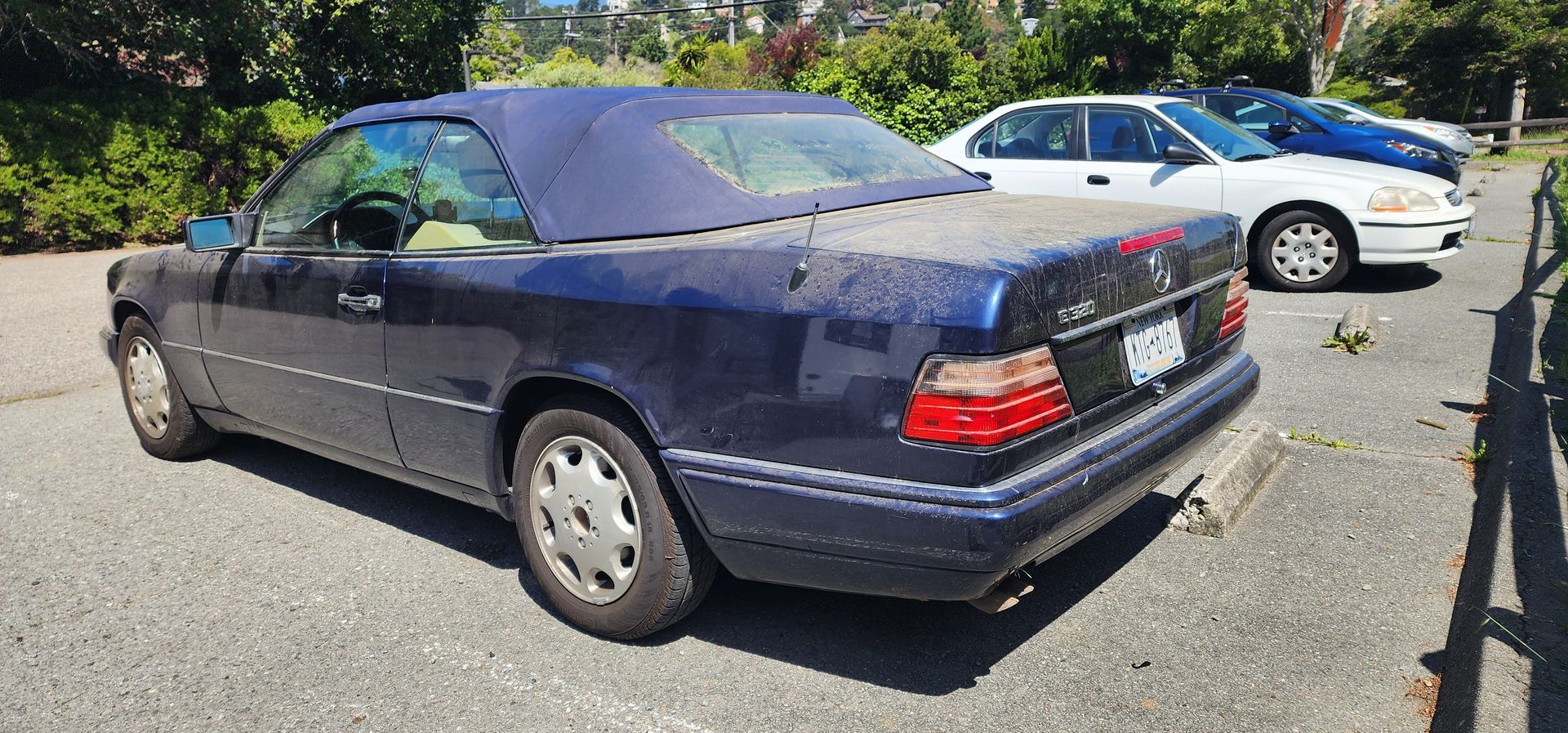 Dark blue sedan parked in a lot, with a white car behind it and a chain-link fence nearby.