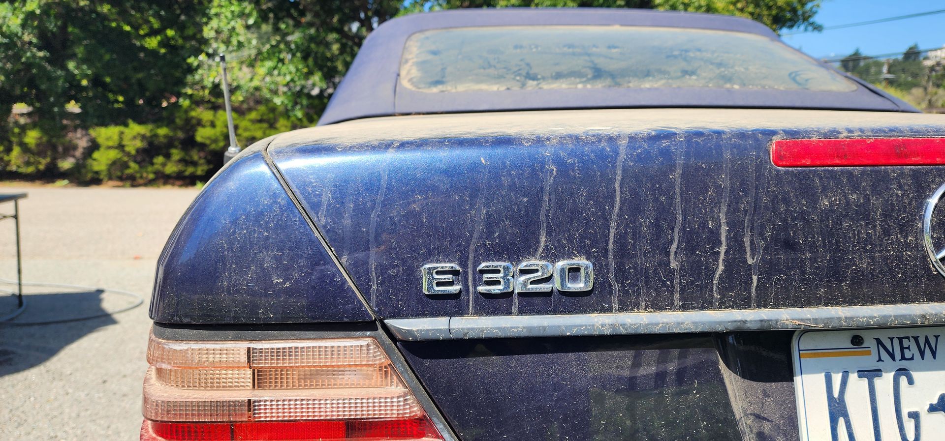 Rear of a dusty blue Mercedes E320 sedan parked outdoors, with a visible New York license plate.