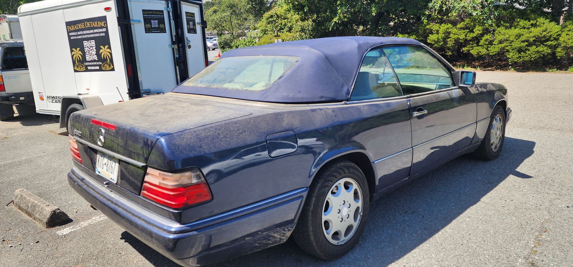 Dark blue Mercedes convertible parked outdoors near a white utility truck in a lot