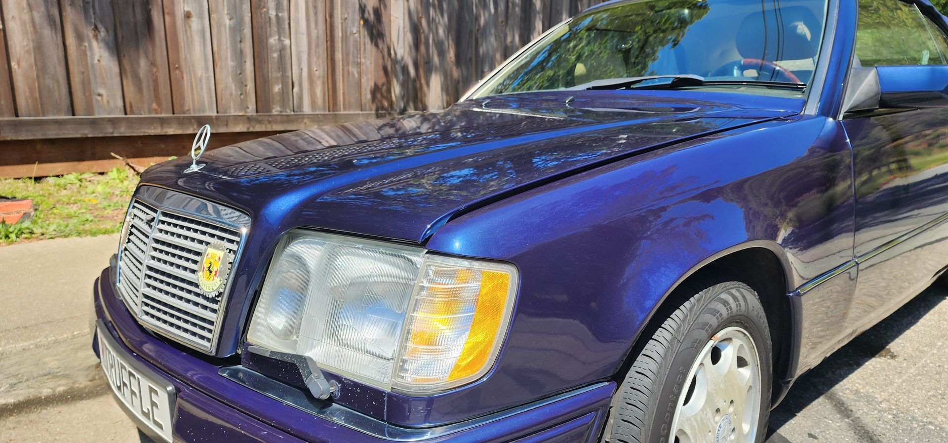 Purple sedan parked outdoors by a wooden fence on a sunny day