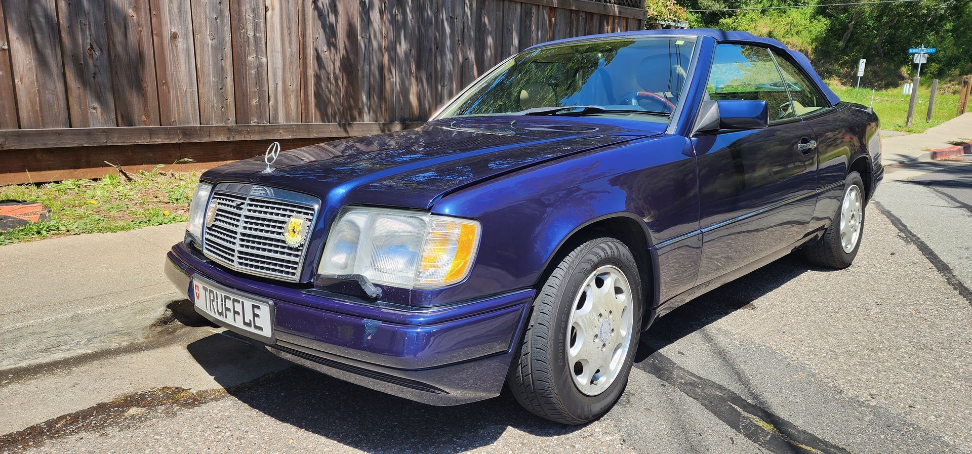 Blue sedan parked on a sunlit street beside a wooden fence