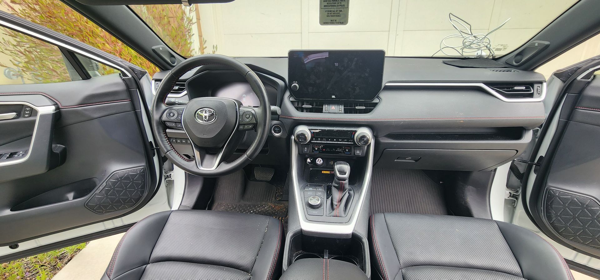 Car interior view with black dashboard, steering wheel, center console, and open front passenger door
