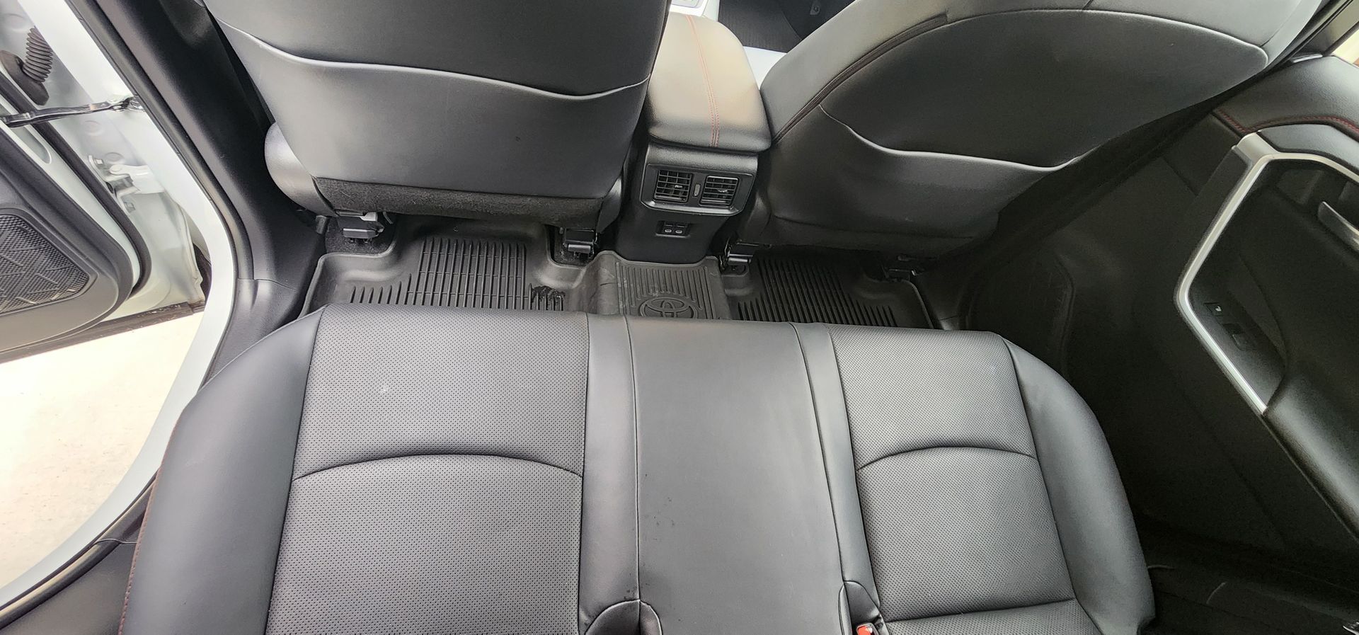 Back seat of a car with black leather upholstery and a center armrest, viewed from above