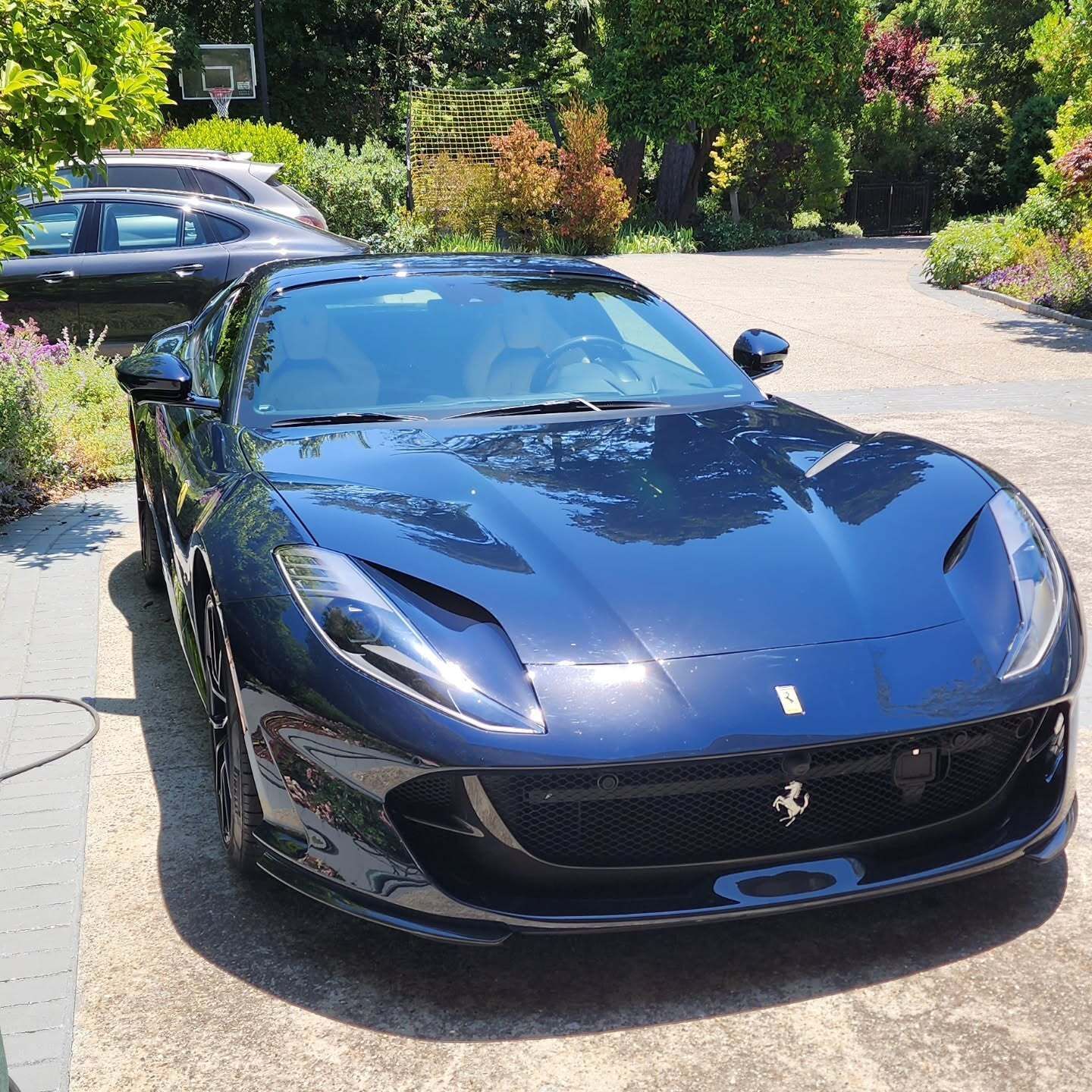 Black Ferrari sports car parked on a driveway in bright sunlight, viewed from the front.