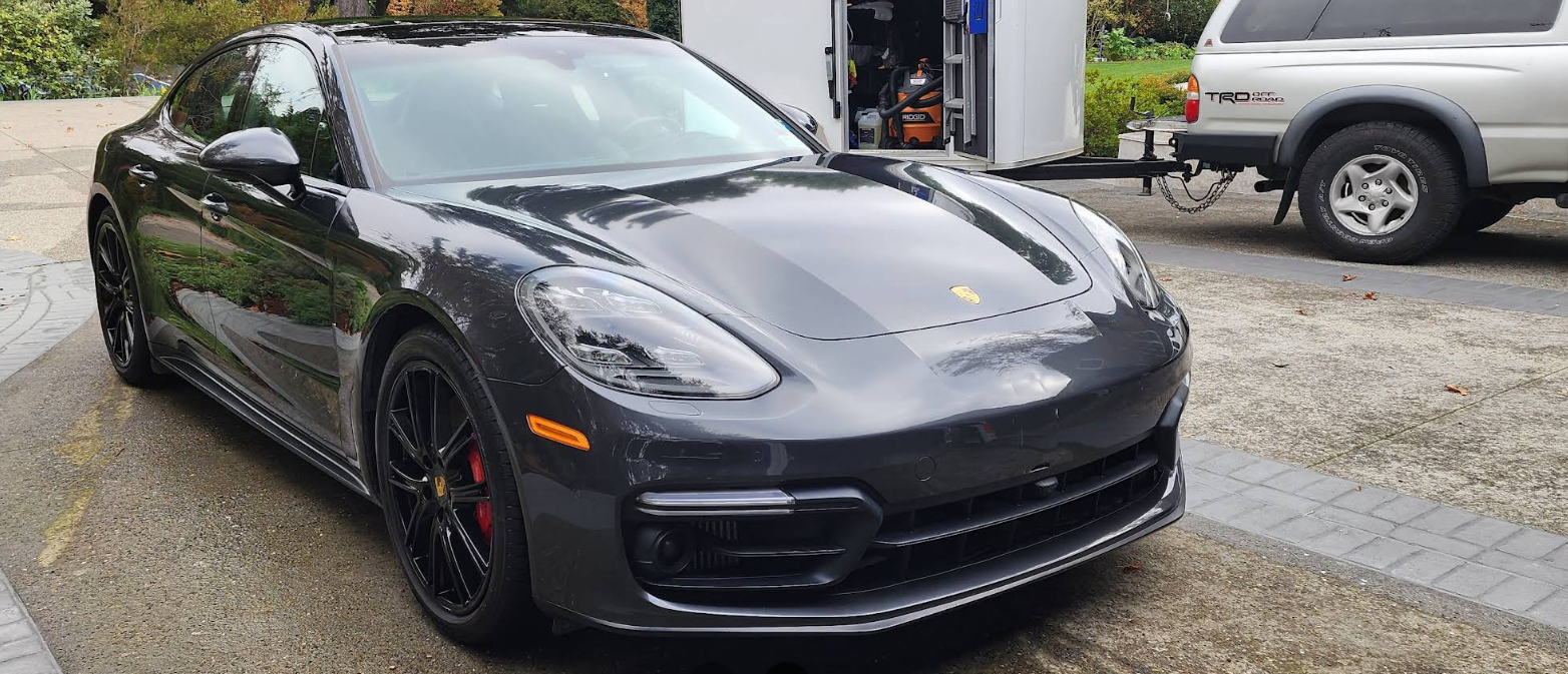 Black sports sedan parked outside a garage on a wet driveway