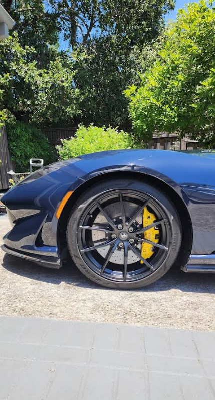 Blue sports car with black wheels and yellow brake calipers parked outdoors in sunlight