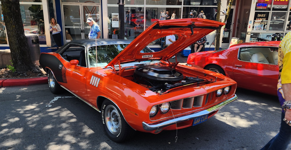 Bright orange classic muscle car with hood open on a city street display