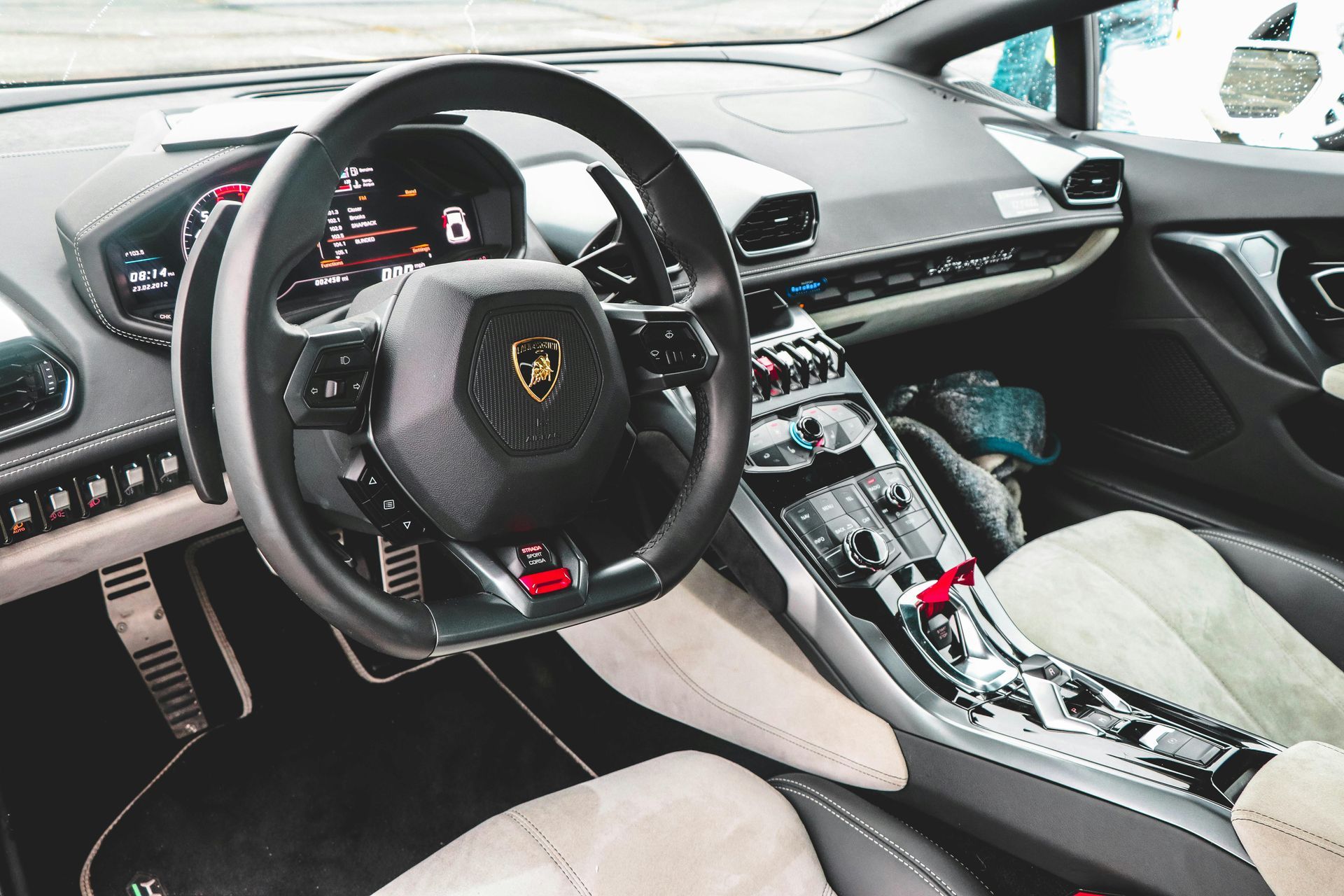 Luxury sports car interior with black steering wheel, beige seats, and exposed metal center console.
