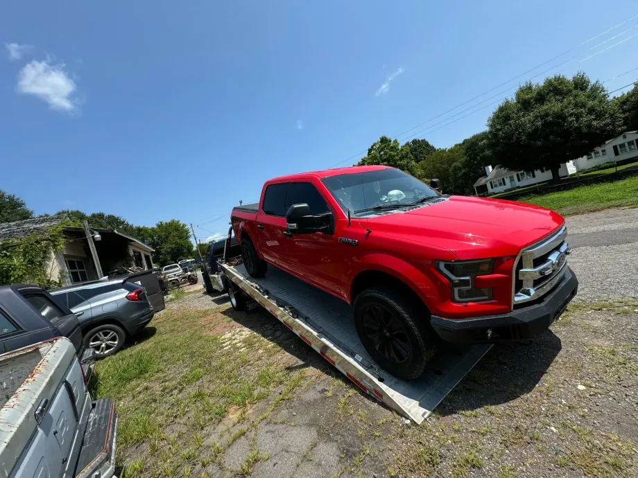 Red pickup truck parked in a lot on a sunny day, with other vehicles nearby and a blue sky.