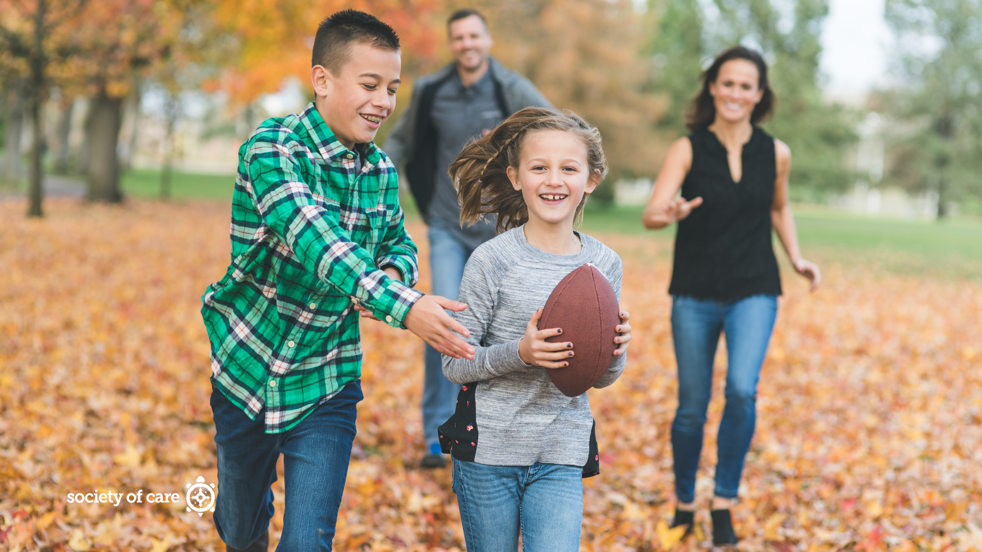 Children and an adult playing catch with a football in a park covered with autumn leaves