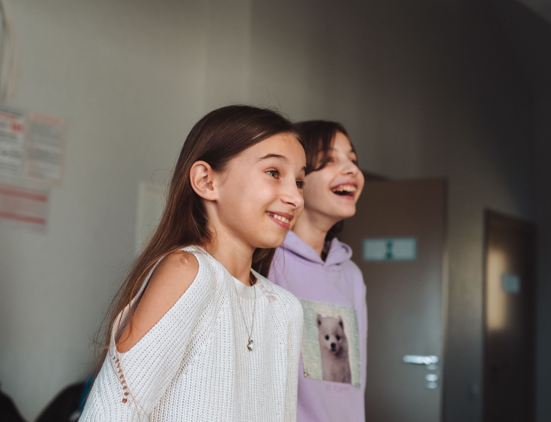 Two smiling children in casual clothes standing indoors near a doorway