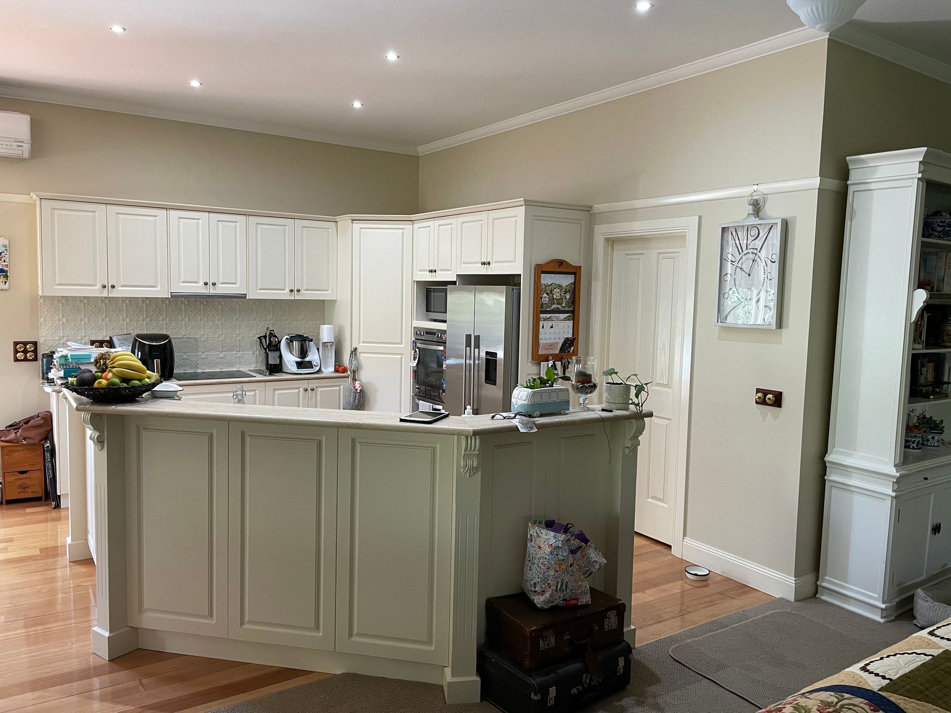 Bright cream kitchen with island, white cabinets, wood floor, and stainless steel refrigerator