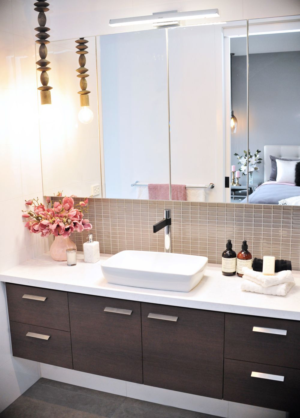 Modern bathroom vanity with white vessel sink, dark cabinets, large mirror, and pink flowers