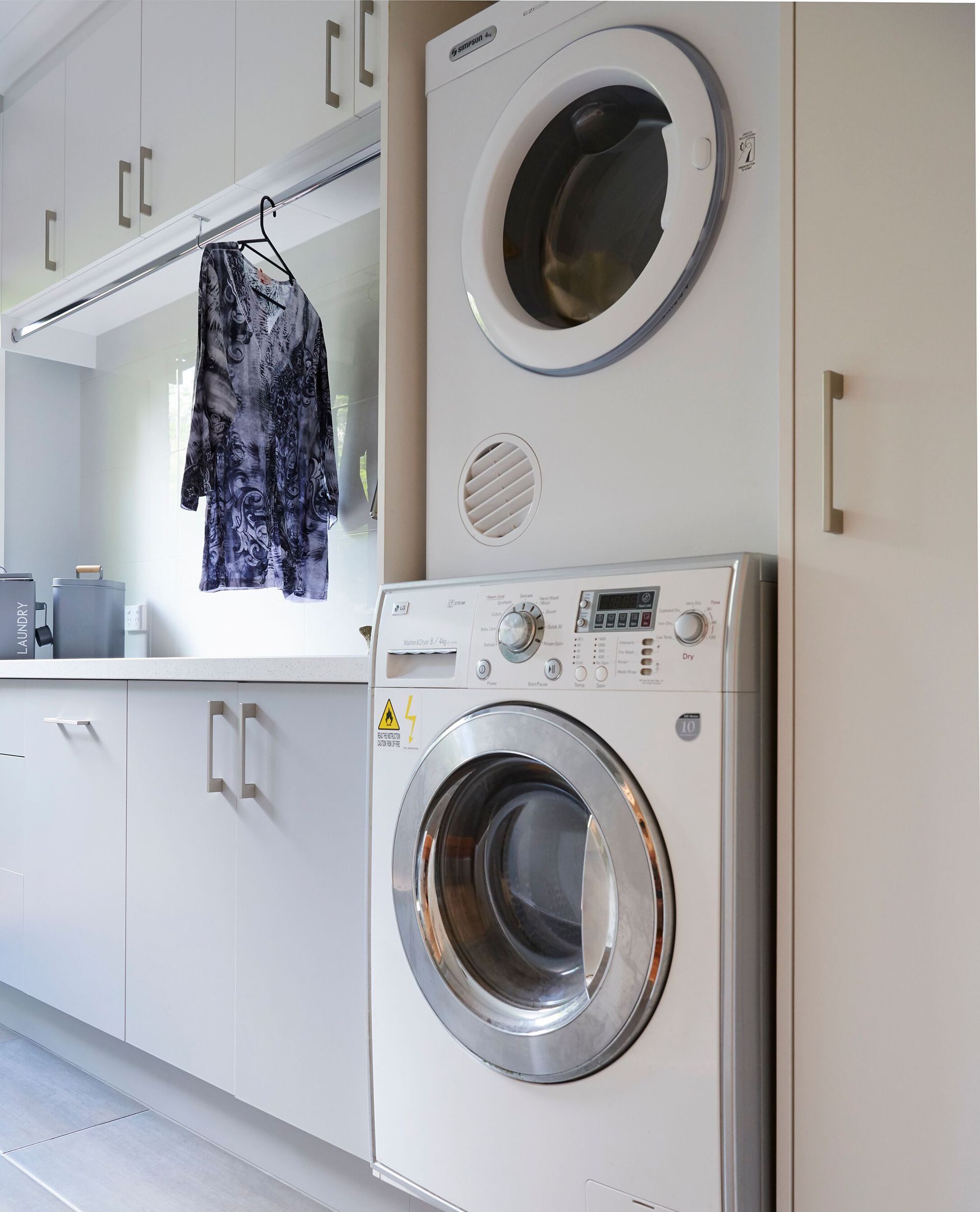 Laundry room with stacked washer and dryer beside white cabinets and a hanging garment.