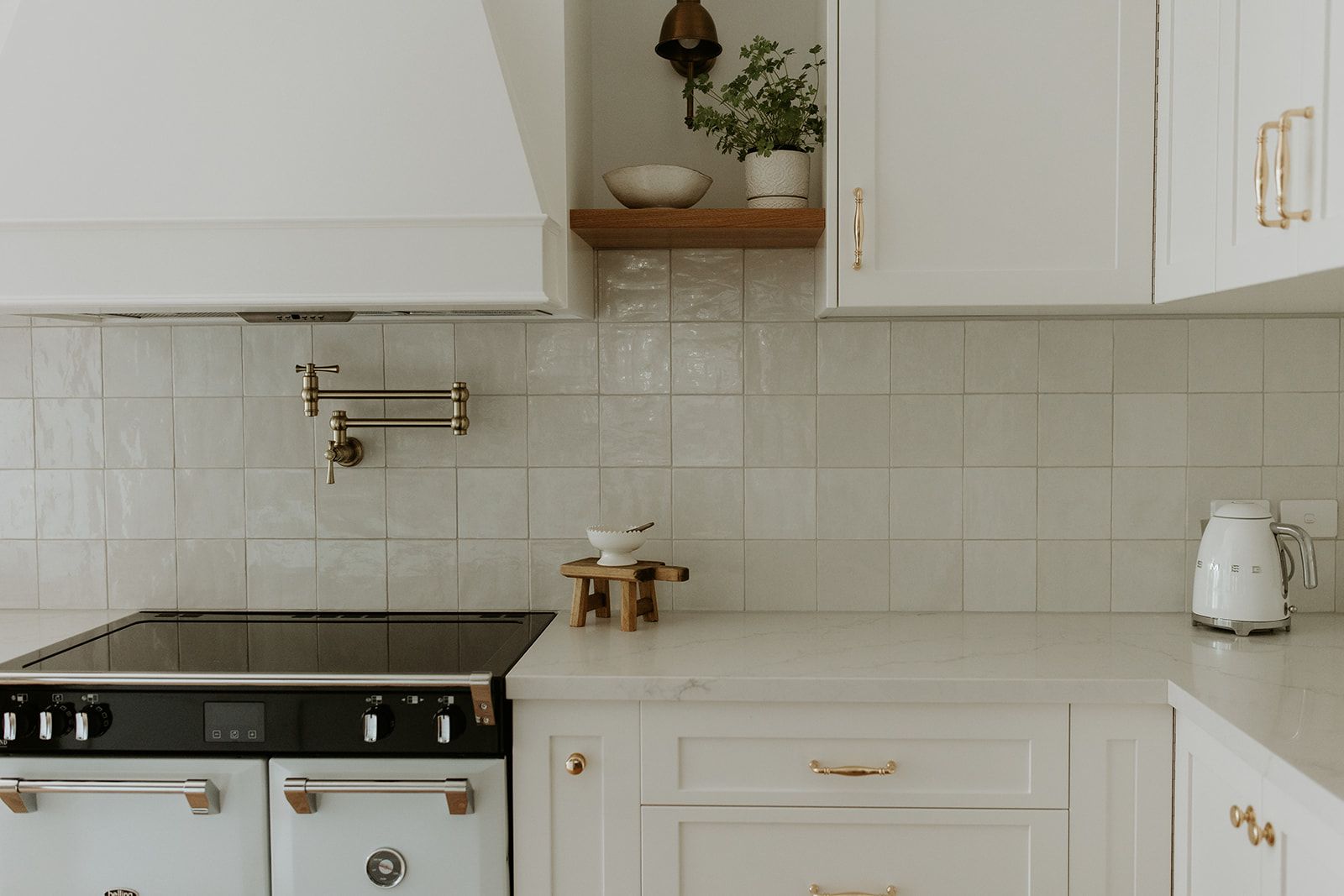 The cooktop wall in a modern country kitchen has pot tapware between the rangehood and cooktop.