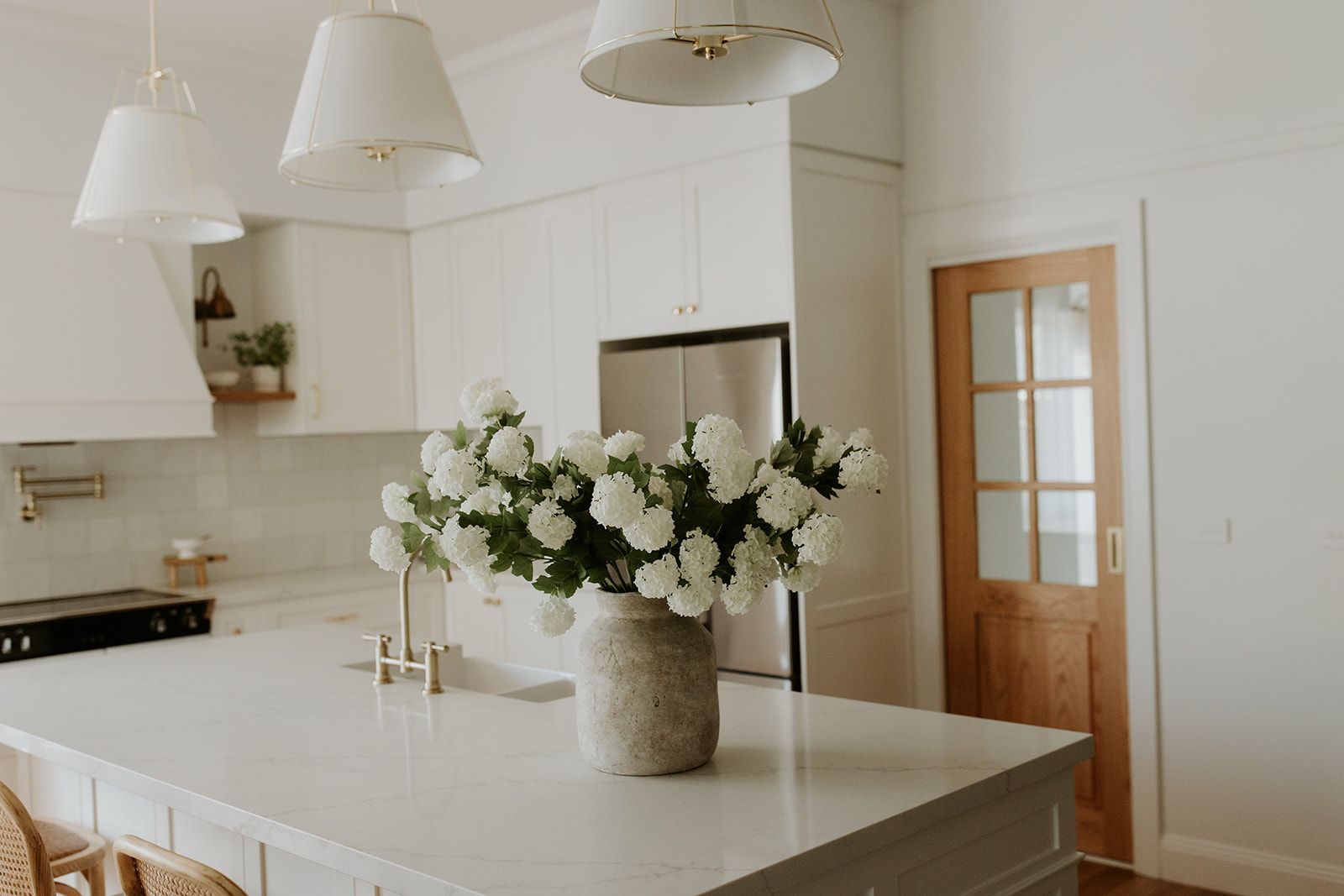 Bright white kitchen with island, pendant lights, and a vase of white flowers on the counter