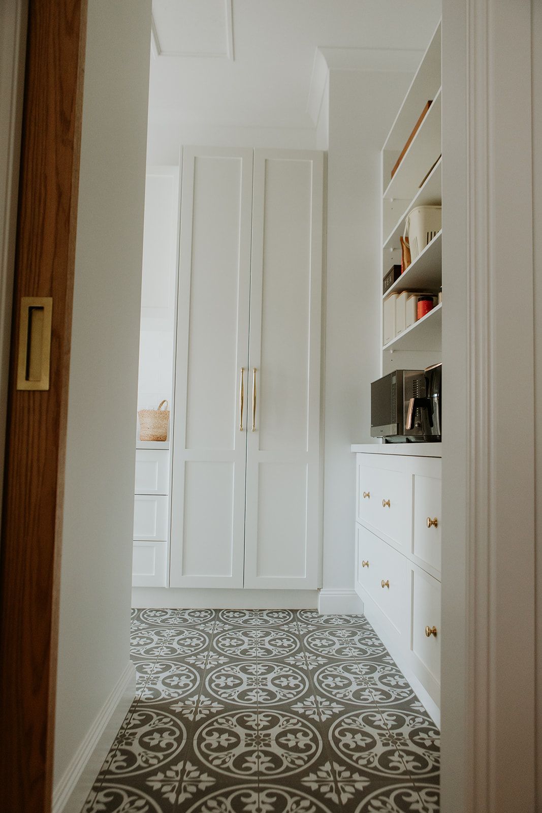 Narrow white hallway with patterned tile floor, built-in shelves, and cabinets leading to a doorway
