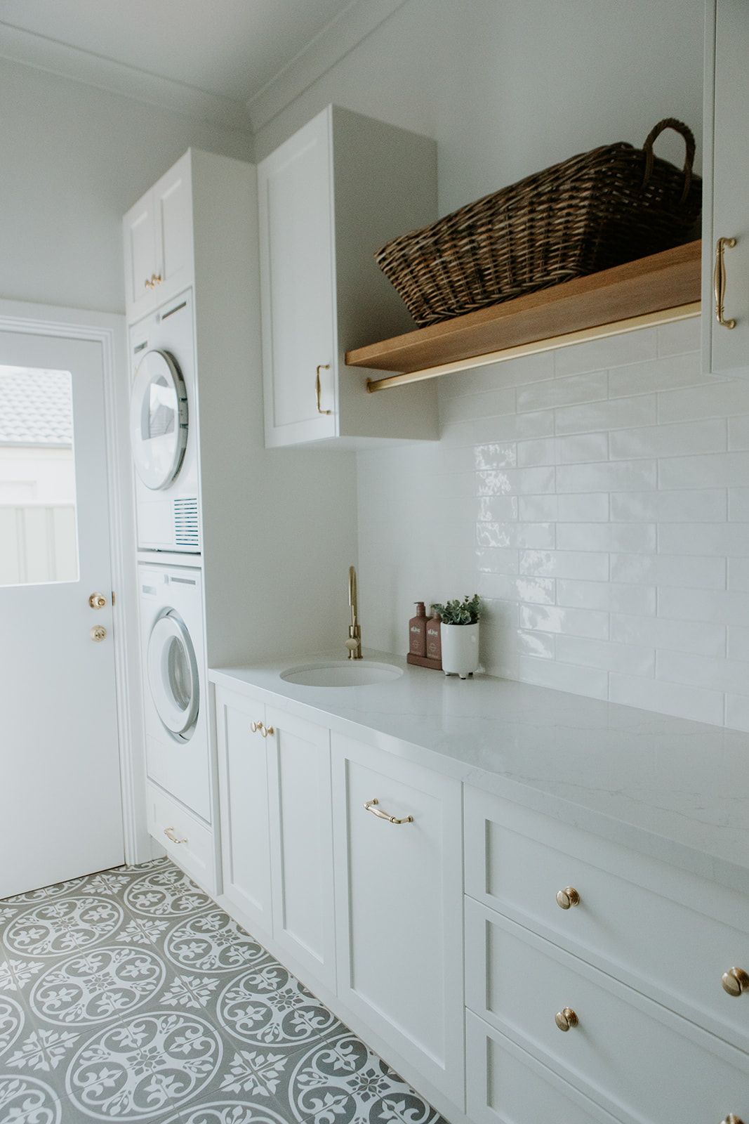 Bright laundry room with stacked washer and dryer, white cabinets, countertop, and patterned tile floor