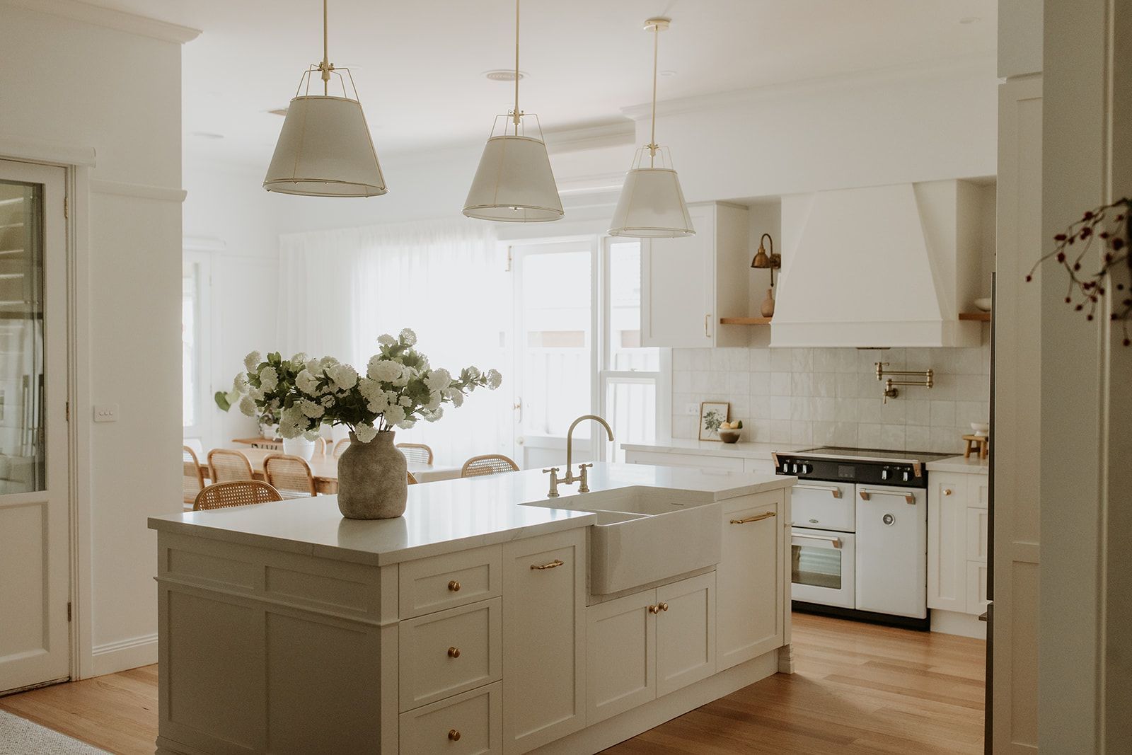 Light-filled white and modern country kitchen. Island has stone benchtop and double farmhouse sink.