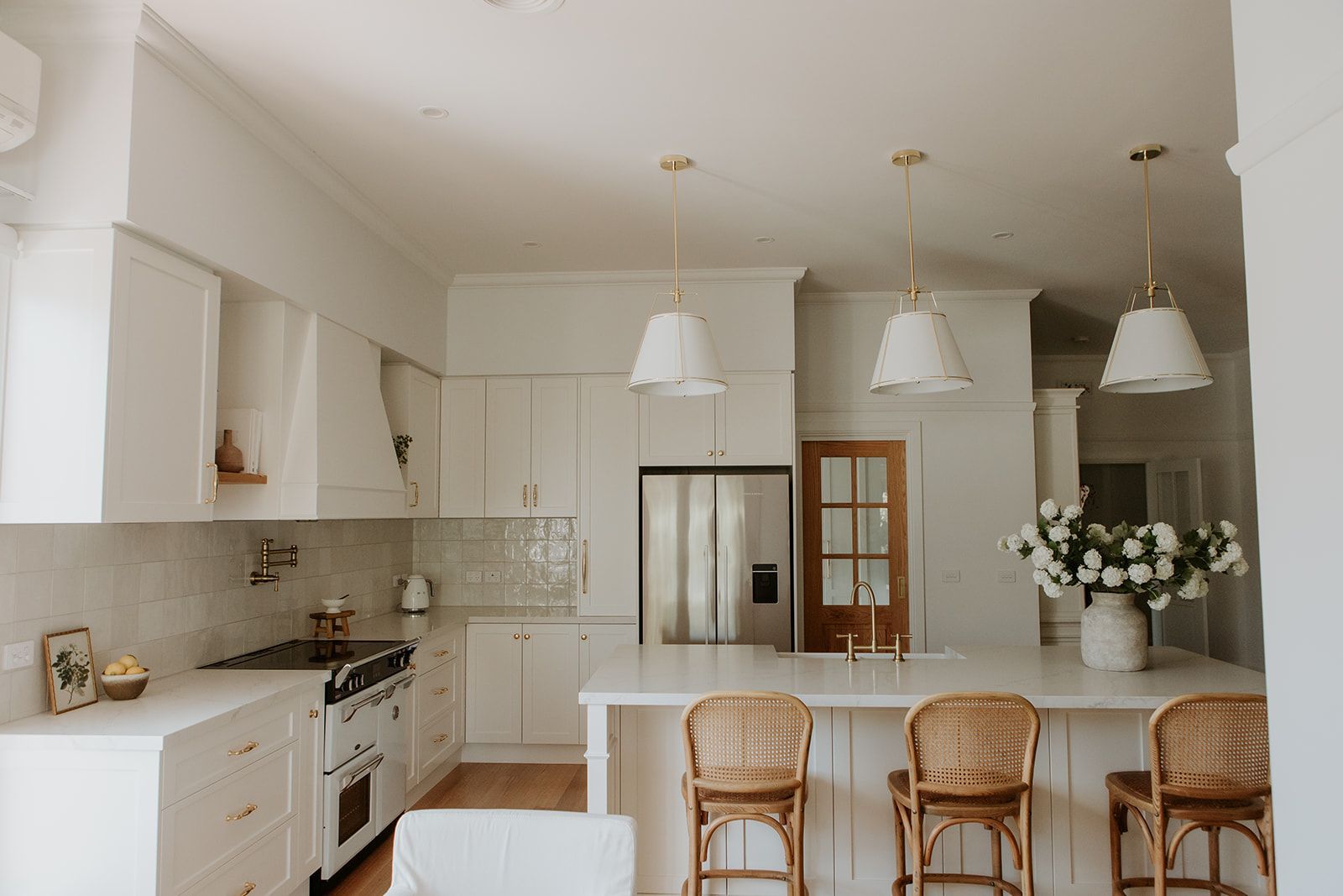 Bright white kitchen with island, wicker stools, pendant lights, and stainless steel refrigerator