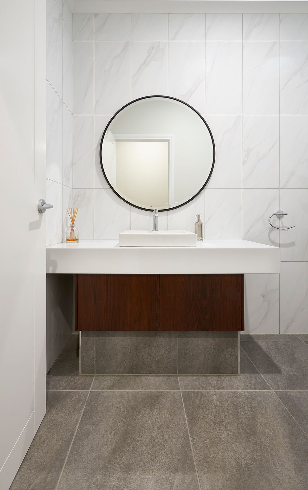 Modern bathroom vanity with round mirror, white sink, and gray tile walls and floor.