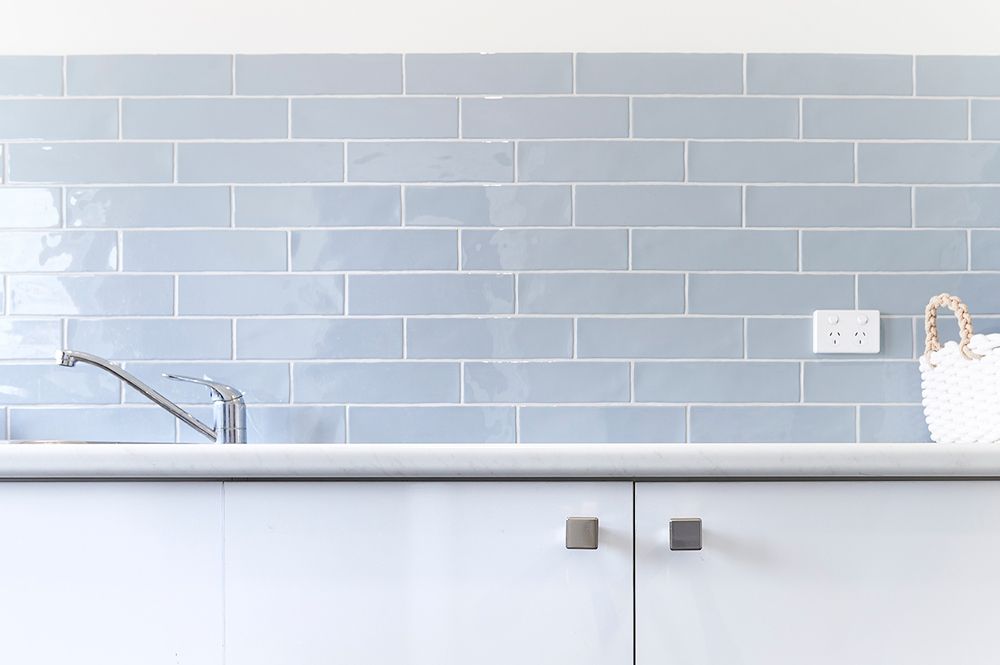 Modern kitchen sink with chrome faucet, pale blue subway tile backsplash, and white cabinets